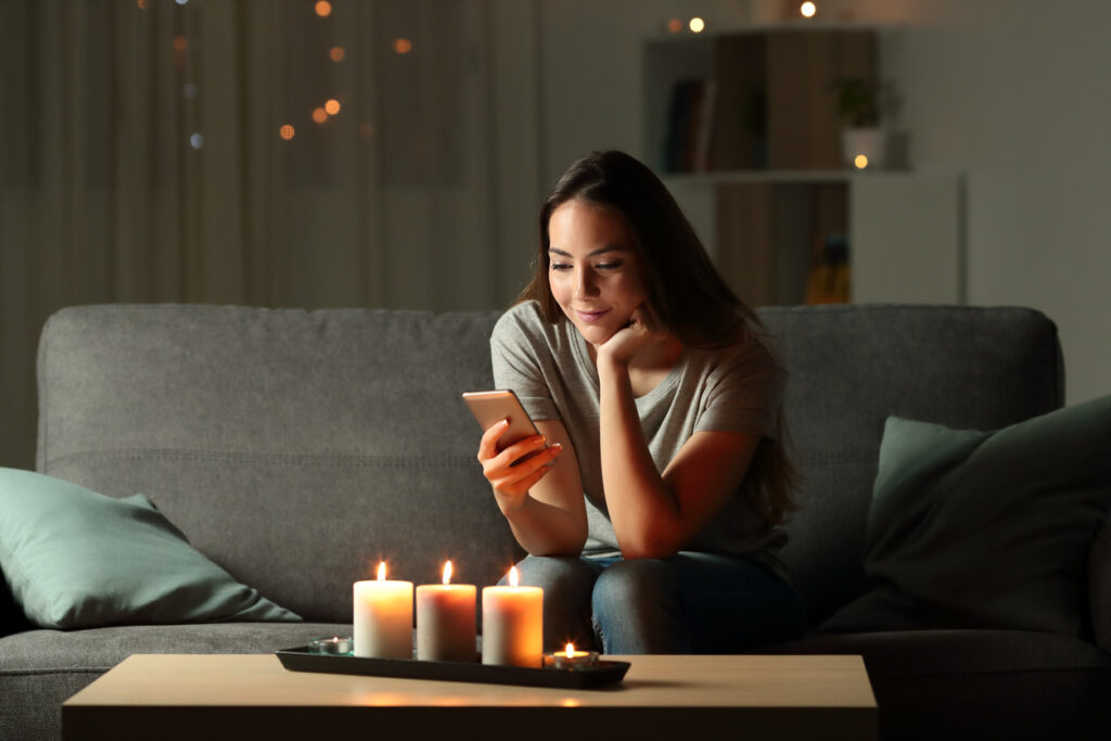 a woman is sitting on a couch with candles and a cell phone.