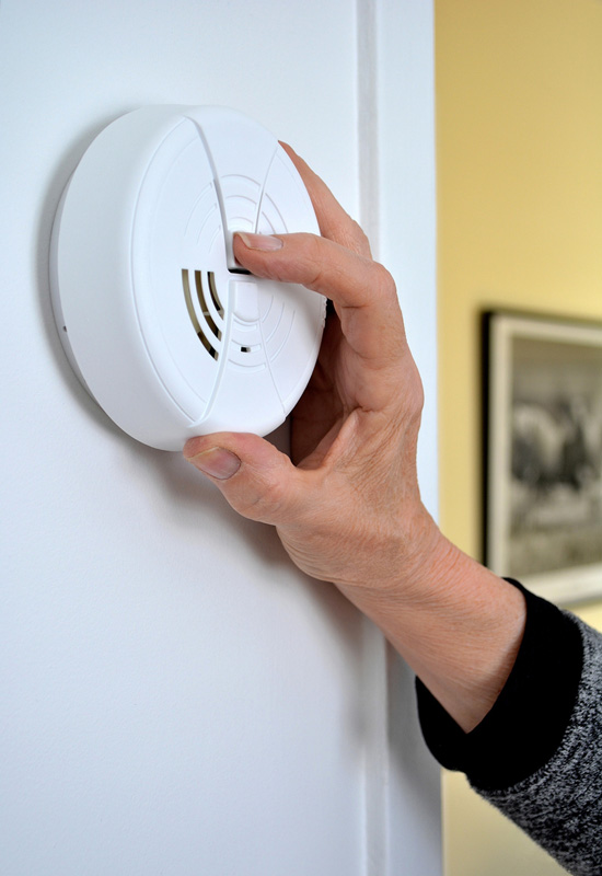 A person turning on a smoke detector on a wall.