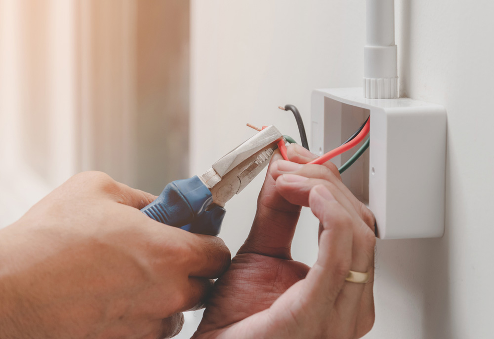 a person is using pliers to connect wires to a wall outlet.